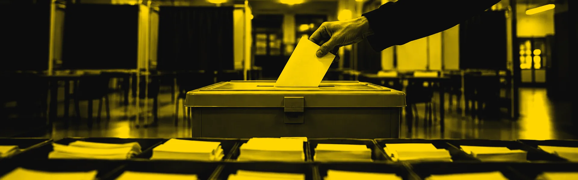 A hand drops a paper ballot into a ballot box at a polling station